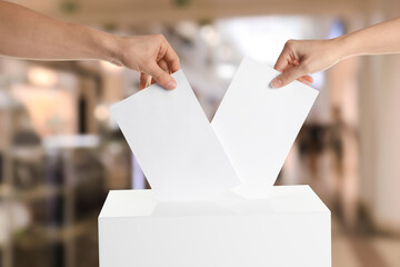 People putting their votes into ballot box indoors, closeup