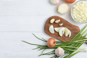 Flat lay composition with cut onion and garlic on white wooden table. Space for text