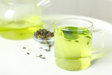Cup of aromatic green tea with leaves on white table