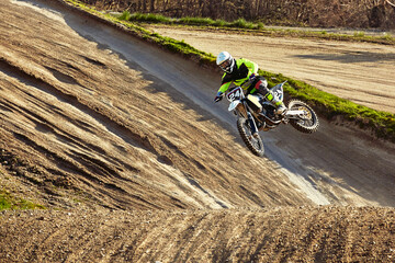 Motocross driver in action accelerating the motorbike takes off and jumps on springboard on the...