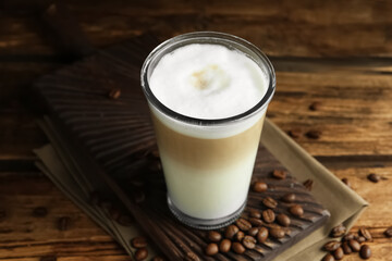 Delicious latte macchiato and coffee beans on wooden table