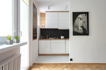 Small kitchen with white furniture and wooden countertop and picture on the wall. Scandinavian interior in apartment with dark marble in the kitchen.