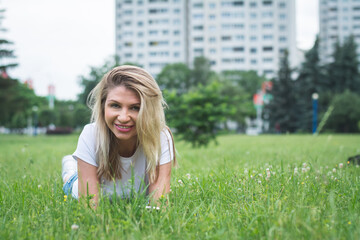 beautiful blonde girl lies on a green lawn in the park and writes a message on her smartphone
