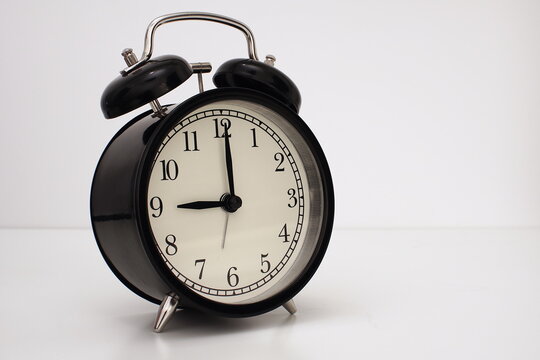 Black vintage alarm clock on table. White background. Wake up concept. An image of a retro clock showing 09:00 pm/am. 