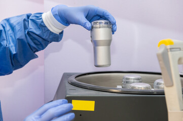 A laboratory technician wearing gloves and a sanitary uniform holds the container with a blood...