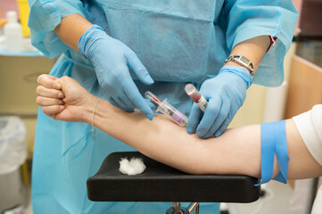 Nurse draws a patient's blood while holding a tube of blood previously drawn for Covid 19 test