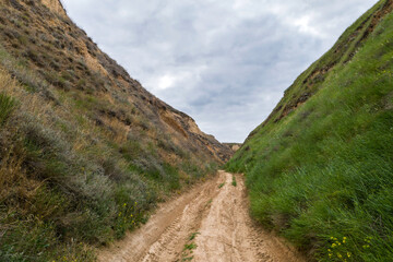 Picturesque view of road between hills with grass on cloudy day