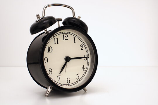 Black vintage alarm clock on table. White background. Wake up concept. An image of a retro clock showing 07:15 pm/am.   