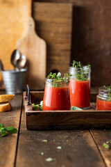 Vegan tomato gazpacho with fresh herbs. Served in glass jars. Rustic, wooden background.