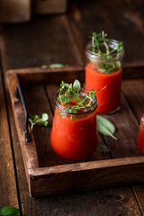 Vegan tomato gazpacho with fresh herbs. Served in glass jars. Rustic, wooden background.