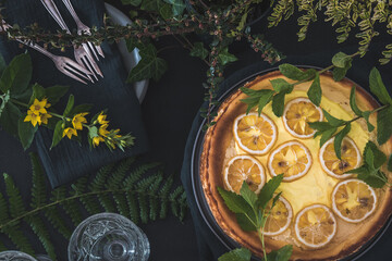 Cheesecake with dried lemon slices and decoration on black background, top view