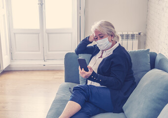 Depressed senior widow woman with protective mask alone at home feeling sad and missing family
