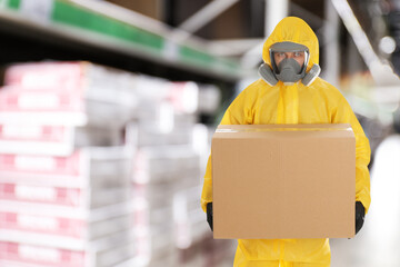 Man wearing chemical protective suit with cardboard box in store. Wholesale market