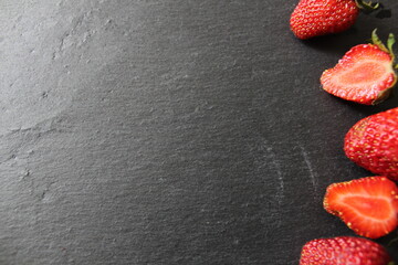 on a black background grey stone there are two halves of strawberries cut on the left side food...