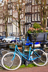 Fototapeta na wymiar Vertical wide daylight view of blue woman's low frame retro bike with white wheels is locked onto the metal railings of a city bridge that crosses a canal in Amsterdam, The Netherlands.