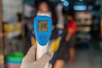 closeup of infrared forehead thermometer (gun) to check body temperature with blurred asian girl on background for Coronavirus, virus symptoms epidemic virus outbreak concept ,Covid-19.