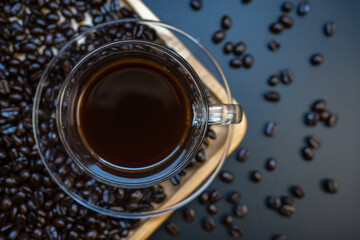 Top view of black coffee in transparent of cup and saucer with coffee beans on wooden tray background.