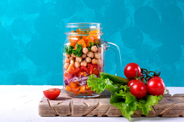 Layered salad with chick peas and vegetables in mason jar against the blue wall