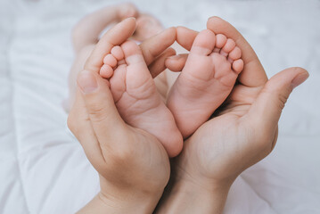 The legs of a small child sleeping on a white bed in the arms of his beloved mother close-up. Woman's happiness. Photography, concept.