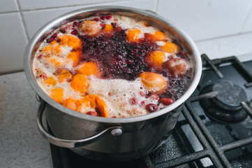 Cooking a delicious compote of apricot, apples, cherries, raspberries. Fresh fruits are boiled in boiling water in a metal pan on the stove. Photography, concept.