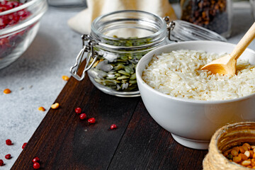 Bowl of dry rice and glass jar with pumpkin seeds on wooden table