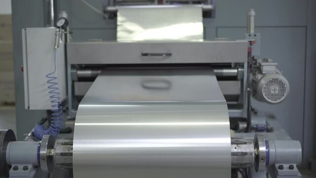 Big roll of aluminium foil sheet rolling on industrial machinery. Equipment working in factory processing raw material. Business, manufacturing, production. Camera moves up.