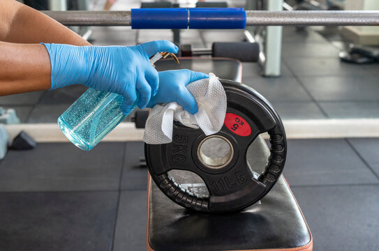 Staff using wet wipe and disinfectant from the bottle spraying weight plate in gym. Antiseptic,disinfection ,cleanliness and healthcare. Anti bacterial and Corona virus COVID19.