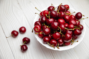 Naklejka na ściany i meble ripe cherries in a white plate on a white wooden background. Vegetarian concept, food. 