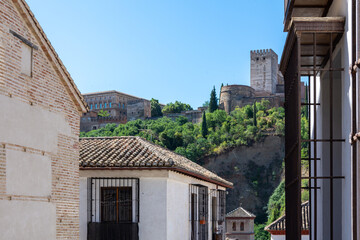 Narrow streets of the Granada neighborhood of Albaicín with the towers of the Alcazaba of the Alhambra in the background