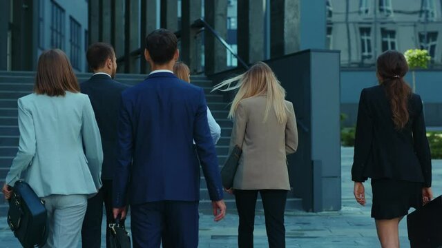 Professional business team of ambitious young office workers going to work entering modern corporate building. Business people. Teambuilding. Collaboration.