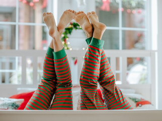 Man's and woman's barefooted legs up in red and green stripped Christmas pyjamas in white room.