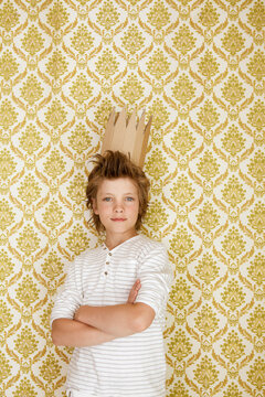 Portrait of a boy standing at a wall wearing cardboard crown