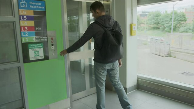 High quality 4k video of a young man who is waiting for elevator on the parking lot or station. men wearing casual clothes and backpack clicking on elevator button and entering elevator doors. 