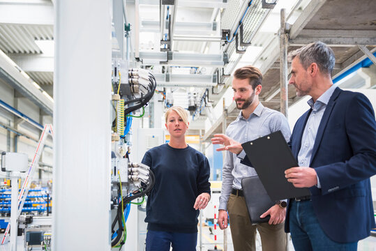 Two men and a woman talking in a factory