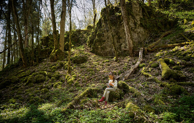 Girl sitting in Swabian Jura forest while using digital tablet during hiking weekend