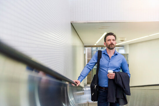 Confident handsome businessman standing with disposable coffee cup on escalator at subway