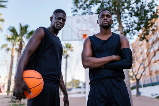 Portrait of young men with basketball standing on basketball court