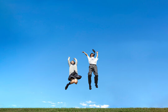 青空を背景にジャンプをする男女高校生