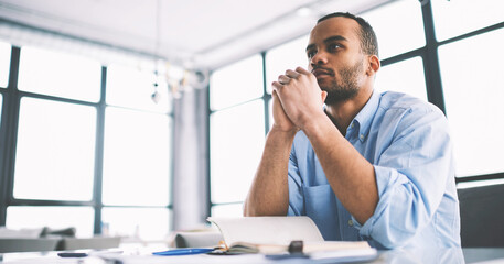 Serious handsome afro american author thinking about ideas for publication sitting at table in...