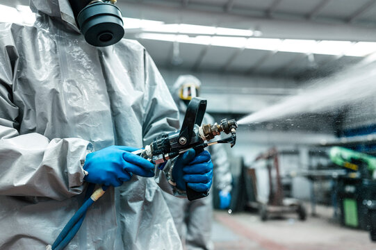 Midsection of disinfection worker spraying decontamination chemical from hose in warehouse