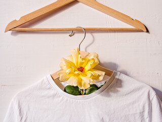Creative floral background. A white cotton T-shirt is hung on a wooden coat hanger and decorated...
