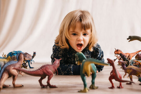 Portrait of little girl lying on the floor playing with toy dinosaurs