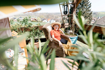 Happy mature woman sitting on  terrace with laptop on lap relaxing