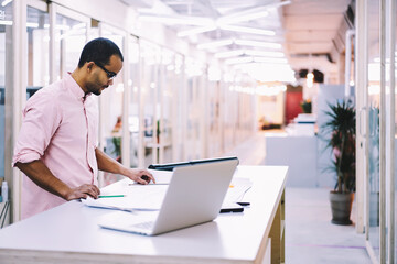 Male talented male student of art faculty of university working on design project creating graphic of building exterior using modern technology and wireless connection to internet in campus indoor