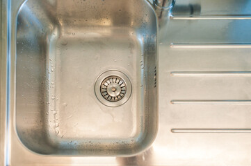 View of a clean sink, drain and running water. Kitchen sink, clean and tidy. Top view, close up