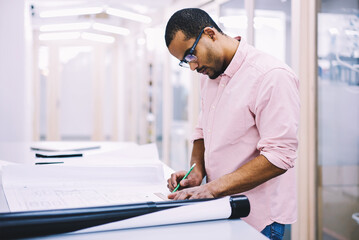 Good looking concentrated creative designer making sketches for building project and reworking...