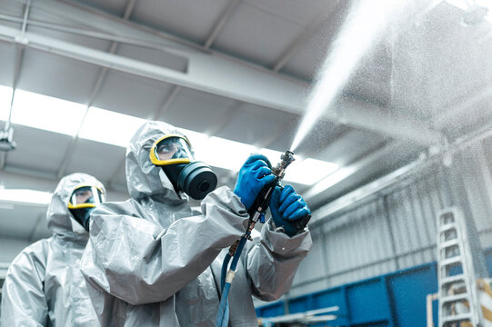 Low angle view of sanitation workers spraying chemical from hose in warehouse