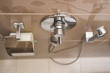 Hygienic shower with faucet and toilet paper on the tiled wall in the toilet. matellic. Close-up