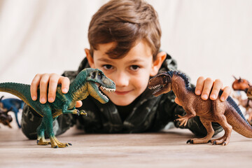 Smiling little boy lying on the floor playing with toy dinosaurs