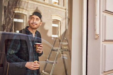 Man refurbishing shop location, drinking coffee, looking out of window